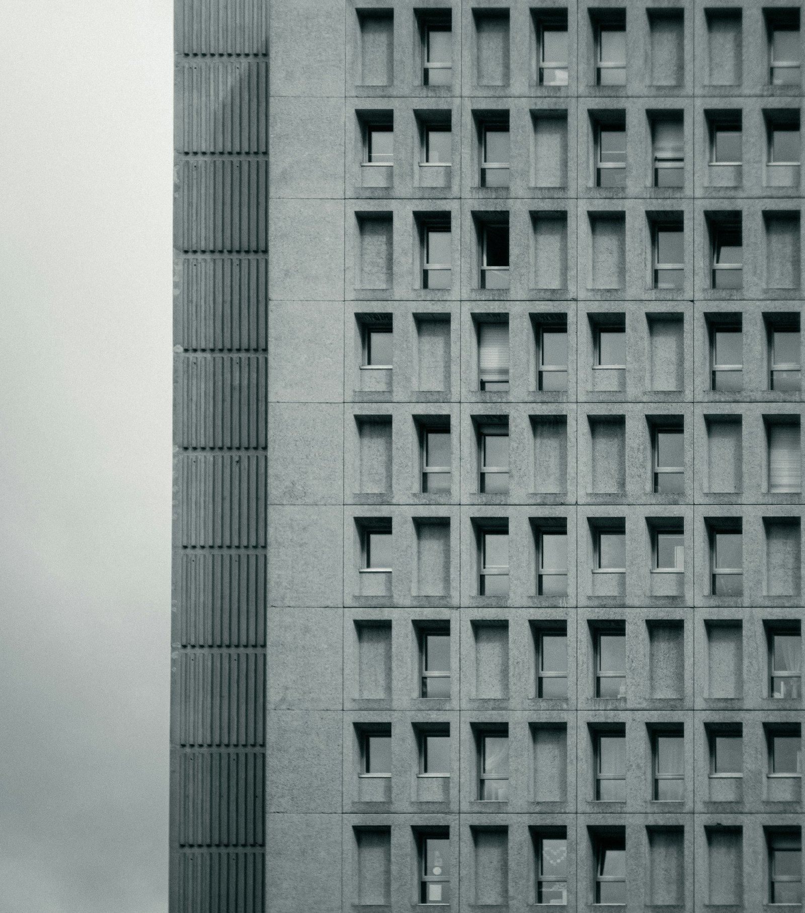 Fachada de concreto brutalista con una retícula de ventanas hundidas, en blanco y negro.